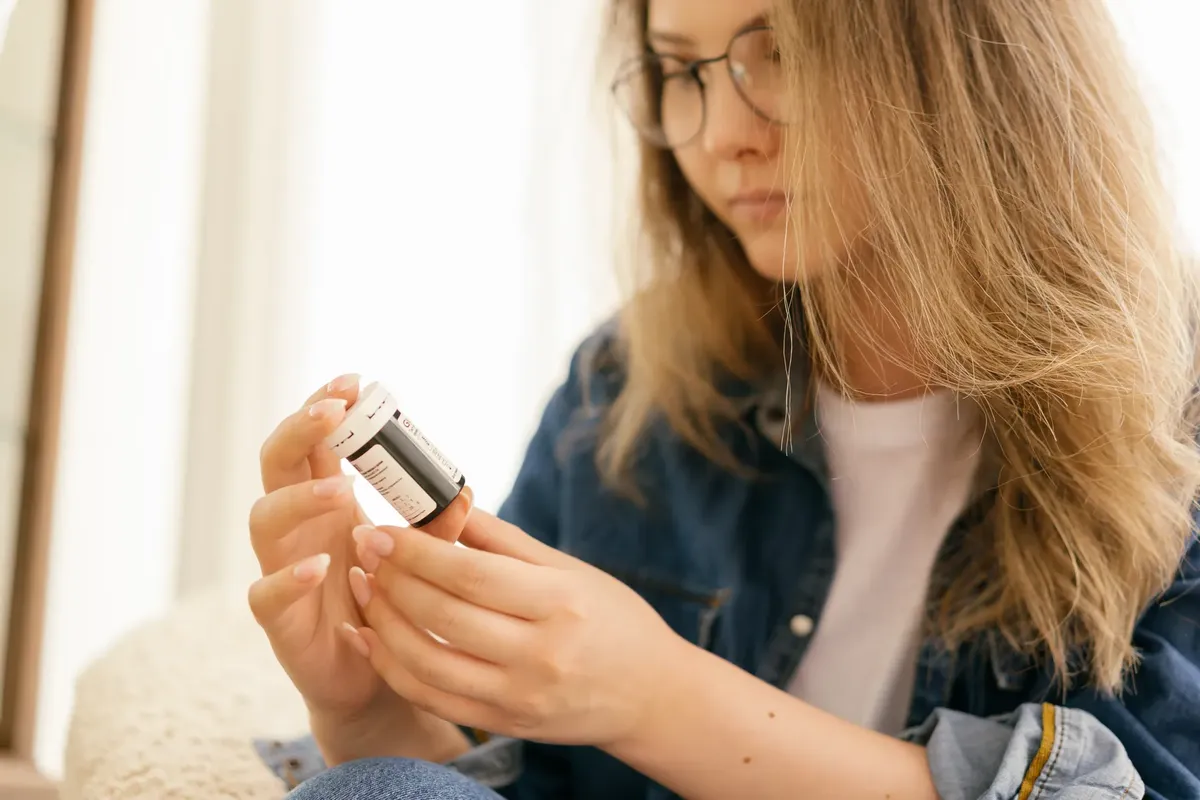 室内で、薬瓶を慎重に見つめている女性で、健康への関心が強調されています。