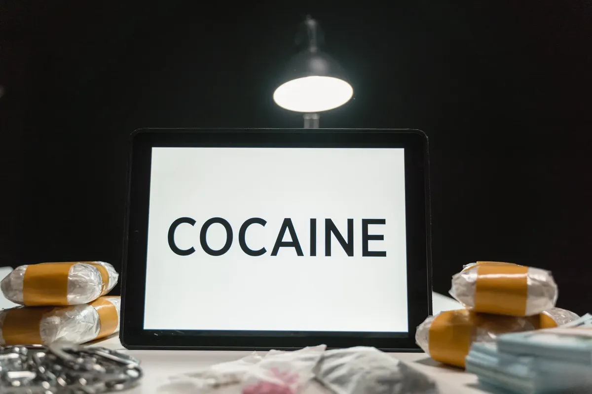 Tablet computer displaying the word 'Cocaine' surrounded by wrapped packets in a dimly lit setting.