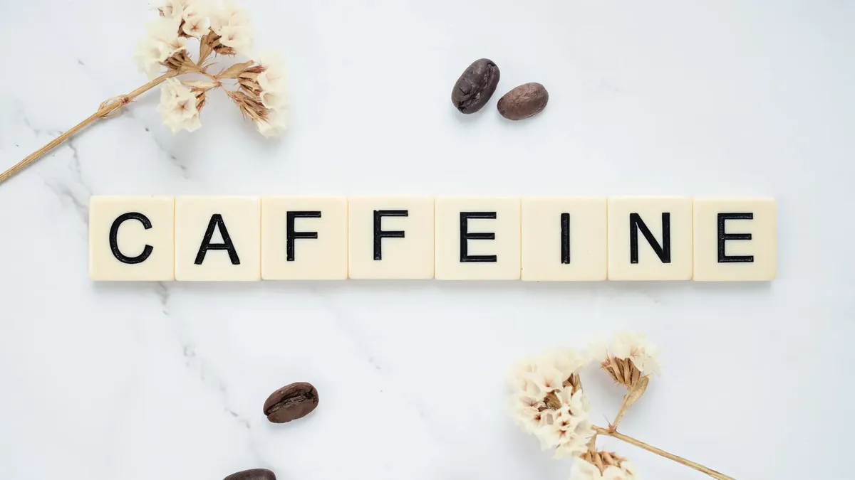Scrabble tiles spelling caffeine with coffee beans on marble background.