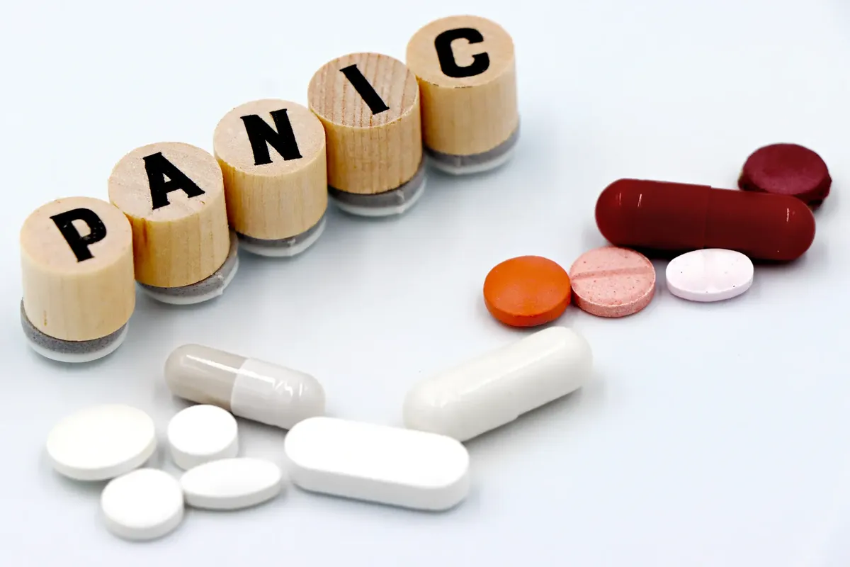 各色藥丸依序排列於木製地磚旁，地磚拼出「PANIC」字，象徵焦慮治療。